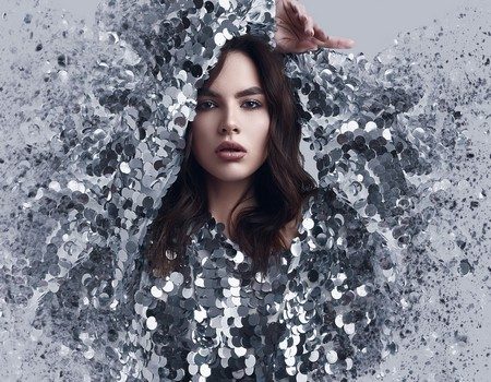 Portrait of a sensual beautiful brunette woman in a shiny fashion dress of sequins with dispersion effect on a white background in studio