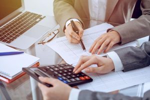 Two female accountants counting on calculator income for tax form completion hands close-up. Business and audit concept.