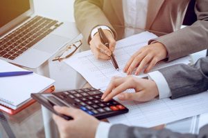 Two female accountants counting on calculator income for tax form completion hands close-up. Business and audit concept Two female accountants counting on calculator income for tax form completion hands close-up. Business and audit concept.